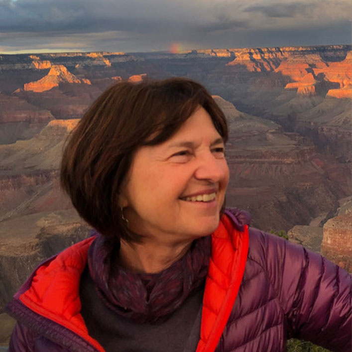 Christine smilling and looking off camera with the sun setting over a red, rocky canyon in the background