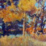 A fall forest landscape in oranges and yellows with a bright blue sky and lake peaking through the foliage