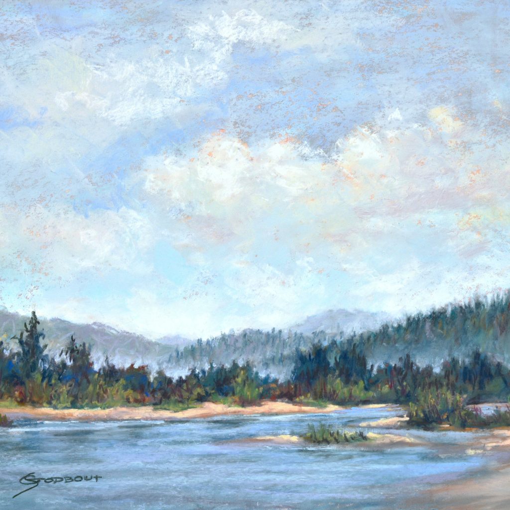 A blue cloudy sky over a light blue lake reflecting the clouds with a tree line and mountains in the distance